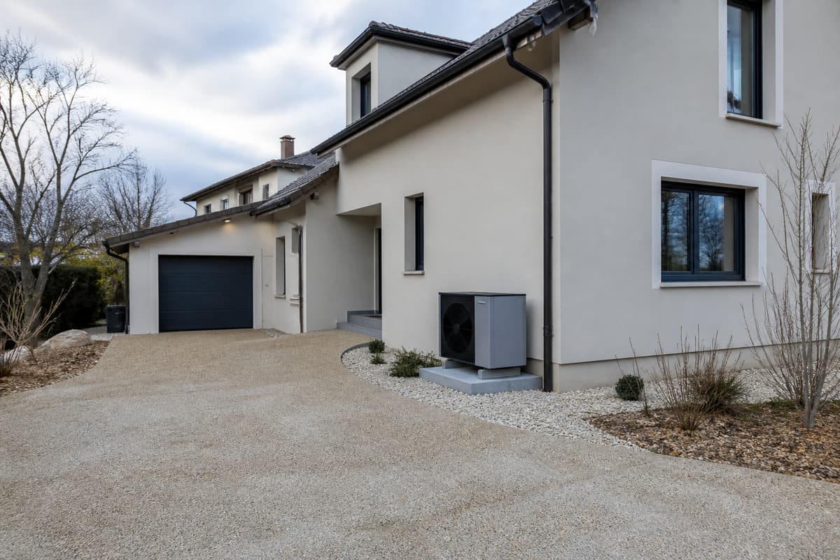 Unité extérieure d'une pompe à chaleur installée discrètement le long de la façade d'une maison individuelle rénovée en hiver.